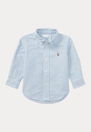 Camisa de niño pequeño de manga larga de color azul claro con cuello abotonado, botones delanteros y pequeño logo marrón bordado en el pecho izquierdo.