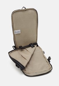 Czarny futerał na zamek z beżowym wnętrzem, wyposażony w miękką wyściółkę, siateczkową kieszeń oraz regulowane klipsy. Kompaktowy, prostokątny kształt.