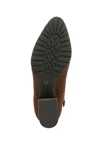 Bottine en suède marron avec une semelle en caoutchouc noir texturé présentant un motif de semelle et un logo VIONIC en relief. Détail de boucle sur le côté inclus.