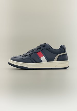 Marineblå sneaker med hvid og rød side stribe, hvid sål og sorte snørebånd på en neutral baggrund.