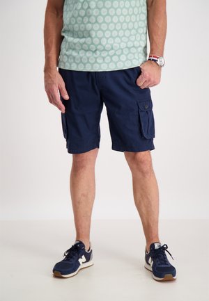 Pantalones cortos de carga en azul marino con dos bolsillos laterales, hechos de una mezcla de algodón. Combinados con una camisa de patrón verde claro y zapatillas en azul marino.