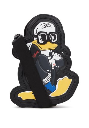 Schoudertas in de vorm van Donald Duck, gekleed in een zwart pak en zonnebril, met gekruiste armen in een zelfverzekerde pose.