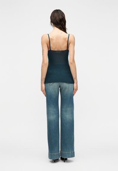 Τιρκουάζ πλεκτό τοπ με λεπτές τιράντες συνδυασμένο με φαρδιά παντελόνια τζιν σε ανοιχτό μπλε, με ξεθωριασμένη όψη και σχεδίαση ψηλής μέσης.
