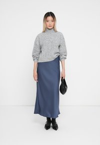 Pulover gri tricotat cu guler înalt, asortat cu o fustă lungă din satin bleumarin. O poșetă neagră tip clutch și pantofi negri cu vârful ascuțit completează ținuta.