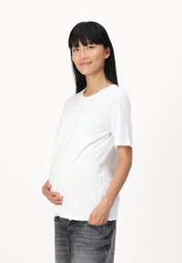 Maglietta premaman bianca con maniche corte, vestibilità comoda, scollo rotondo e tessuto morbido. Abbinata a jeans grigi.