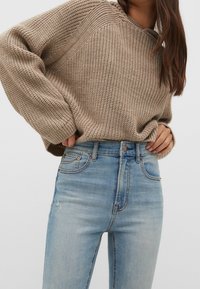 Beige knitted sweater with oversized sleeves paired with light blue high-waisted jeans featuring slight distressed details and copper hardware.