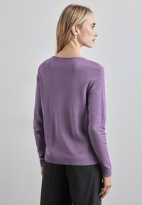 Lila långärmad tröja med rund halsringning, ribbad nederkant och slät textur, i kombination med mörkgrå vida byxor.