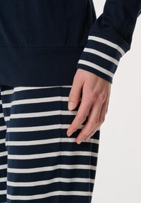 Marinblå och vitrandig loungekläder-set. Toppen har långa ärmar i enfärgad marinblå; byxorna har vita ränder på en marinblå bakgrund, gjorda av mjuk bomull.