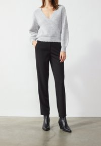 Gray, knit wrap sweater with a deep V-neck, paired with black, tailored trousers and black heeled ankle boots. Smooth textures and fitted design.