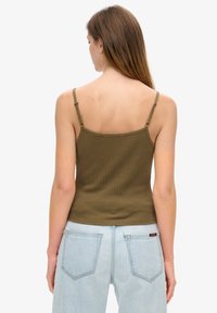 Oliwkowy, prążkowany top na ramiączkach z cienkimi, regulowanymi paskami i dopasowanym krojem. Tył ma czerwony detal szycia w okolicy dekoltu.