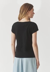 Maglietta nera a maniche corte con scollatura rotonda e dettagli di cucitura sottili, abbinata a pantaloni larghi blu chiaro.