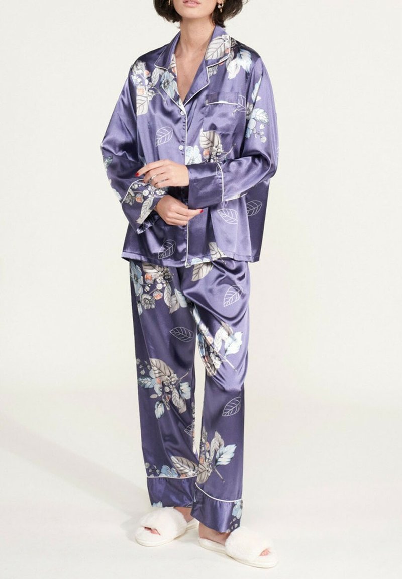 Ensemble de pyjama en satin de couleur violet foncé avec des motifs floraux, comprenant un haut à boutons et un pantalon assorti, avec des détails en piping blancs et une coupe décontractée.