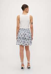 Top blanco sin mangas combinado con una falda estampada en azul y blanco, con un dobladillo con volantes y tacones negros con tiras.