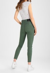 Zielone dżinsy slim fit z średnim stanem, z detalami w postaci przeszyć i tylną kieszenią. Połączone z krótkim topem w paski i białymi sneakersami.