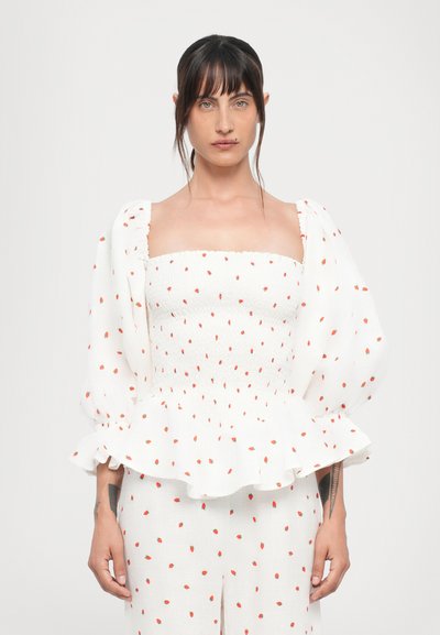 Blusa blanca con patrón de puntos rojos, escote cuadrado, mangas abullonadas, cuerpo fruncido y dobladillo tipo peplum. Tejido ligero con una textura sutil.