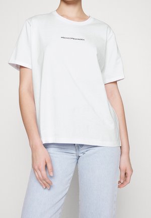 Maglietta bianca in cotone con maniche corte, scollatura rotonda e logo frontale "MSCHCOPENHAGEN" in nero. Abbinata a jeans azzurri.