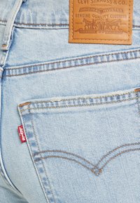 Light blue denim jeans feature a leather tag embossed with "Levi Strauss & Co." and a red tab on the back pocket, with orange stitching accents.