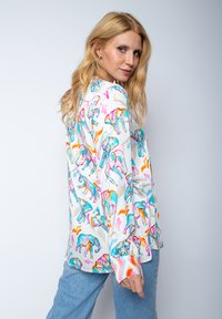 Langarmshirt mit einem mehrfarbigen Elefantenmuster auf weißem Hintergrund. Hergestellt aus leichtem Stoff mit lockerer Passform.