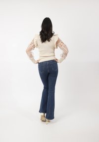 Maglione beige a coste con maniche in pizzo trasparente, in evidenza di ruffled. Abbinato a jeans blu svasati e scarpe con tacco alto.