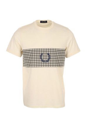 T-shirt beige à manches courtes avec une bande à motif quadrillage noir et blanc sur la poitrine, avec un logo couronne de laurier bleu marine au centre.