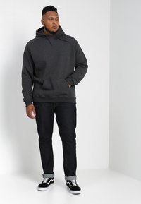 Grå hettegenser med kengurulomme, med snor til hetten. Kombinert med mørke jeans og svarte joggesko med hvite såler.