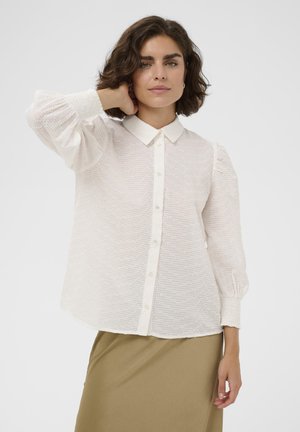 Biela blúzka s textúrovaným vzorom, zapínaním na gombíky vpredu a nadýchanými rukávmi. Má klasický golier a elastické manžety.