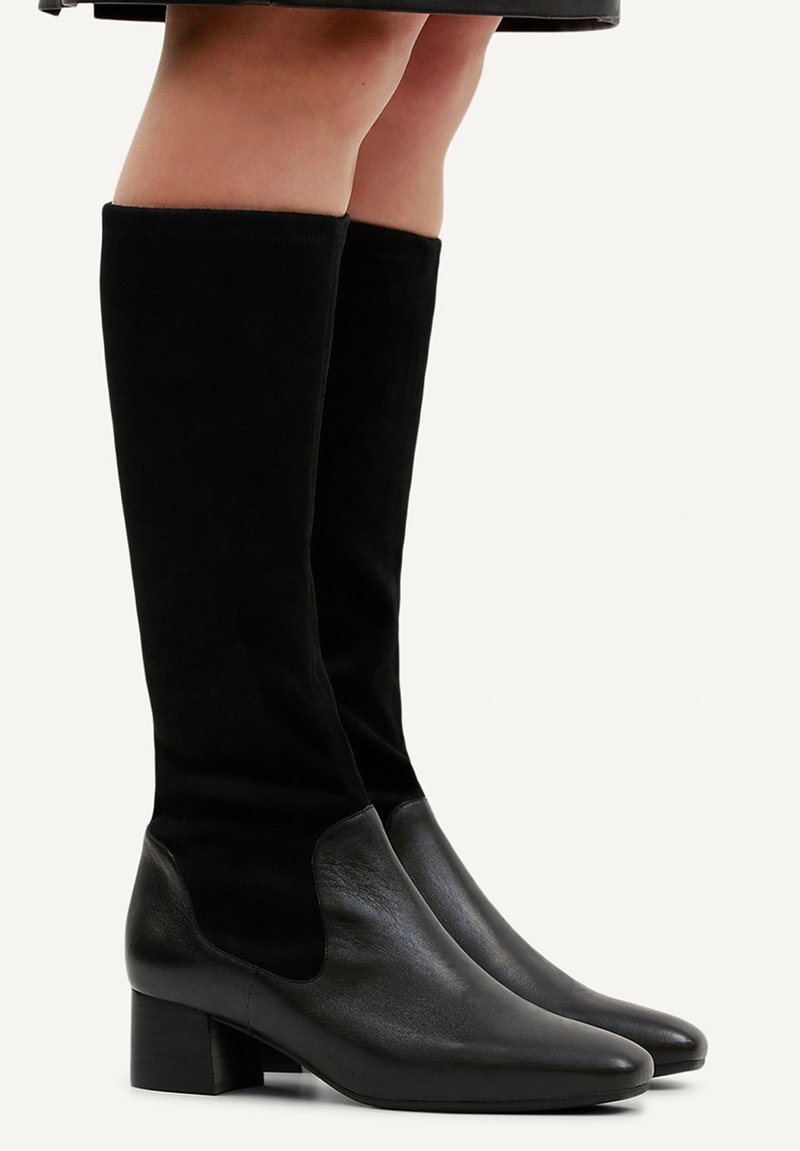 Knöchelhöhe schwarze Wildlederstiefel mit Lederakzenten, runder Zehenpartie und Blockabsatz. Das Obermaterial ist glatt mit einer weichen Textur.