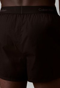 Czarne kąpielówki wykonane z lekkiego materiału, z elastycznym pasem i brandingiem "Calvin Klein". Design jest prosty i funkcjonalny.