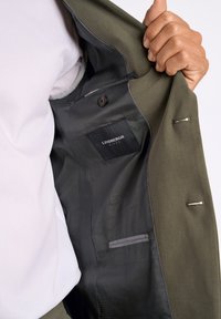 Olijfgroene blazer met zwarte voering. Bevat een binnenzak en knoopsluiting. Gladde textuur, strakke ontwerp en getailleerde pasvorm.
