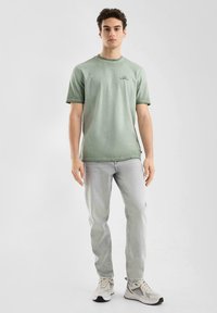 T-shirt rayé vert en tissu doux, associé à un jean gris clair. Chaussures gris clair avec des accents noirs. Design simple avec peu de détails.