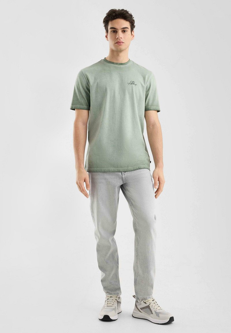 T-shirt rayé vert en tissu doux, associé à un jean gris clair. Chaussures gris clair avec des accents noirs. Design simple avec peu de détails.