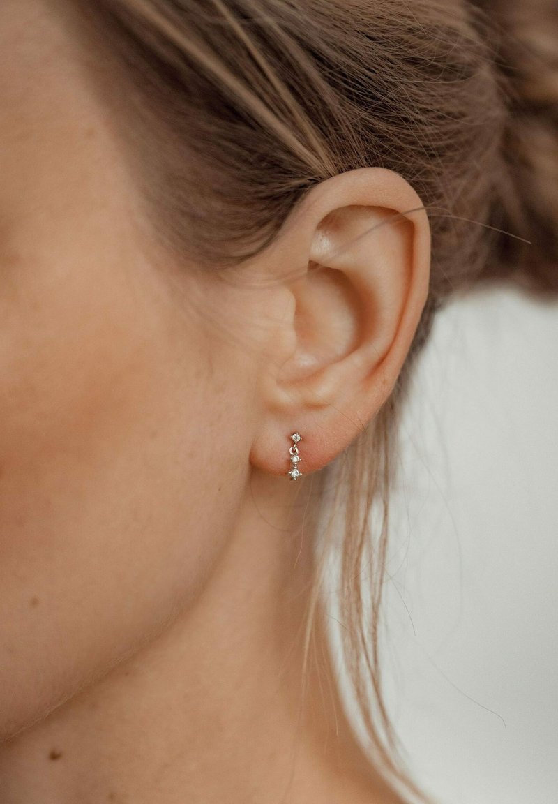 Pendientes de plata con tres diamantes verticales, dispuestos con un acento circular y en forma de estrella, que exhiben un diseño delicado y minimalista.