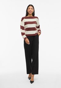 Sweater riscado em creme e bordô, ajuste relaxado com punhos canelados. Combinado com calças largas pretas e saltos agudos pretos.