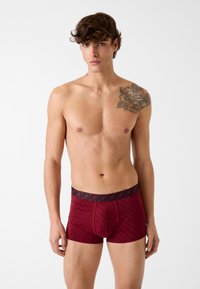 Boxer shorts a fantasia rossa con una cintura elastica nera. Il materiale sembra liscio, con un motivo a diamante presente in tutto il tessuto.