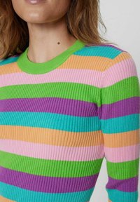 Donna che indossa un maglione a coste con strisce orizzontali verdi, viola, rosa, arancioni e turchesi, mostrando il collo e la parte superiore del torso.