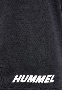 Shorts de sport noirs en tissu texturé, avec un ourlet incliné et un logo blanc "HUMMEL" bien visible sur le côté inférieur droit.