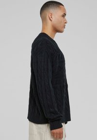 Pull en maille torsadée bleu marine foncé avec manches longues, présentant un motif texturé et des poignets côtelés. Coupe décontractée et col rond.