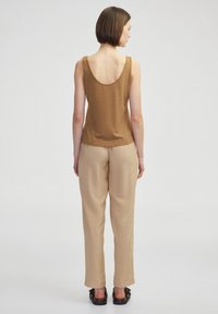Top corto marrone con scollatura a giro, abbinato a pantaloni beige a gamba larga. Il modello indossa sandali scuri. Tessuto semplice e liscio.