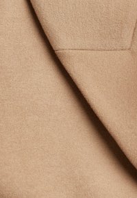 Hellbrauner Wollstoff mit einer weichen, glatten Textur, der ein gefaltetes Design mit einem subtilen Glanz und ohne sichtbare Muster zeigt.