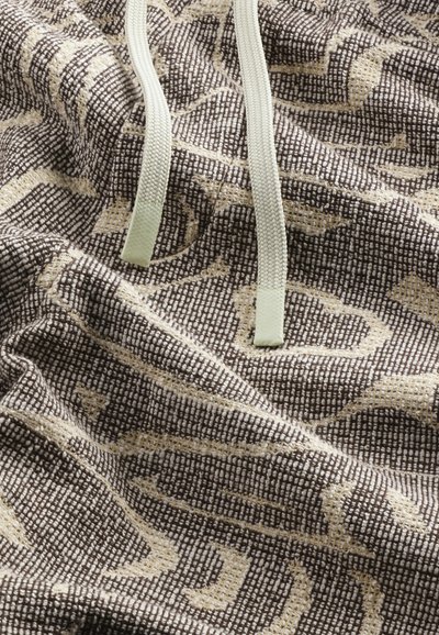 Flätad brun tyg med beige geometriska mönster; har ljusgröna snoddar och en strukturerad yta.