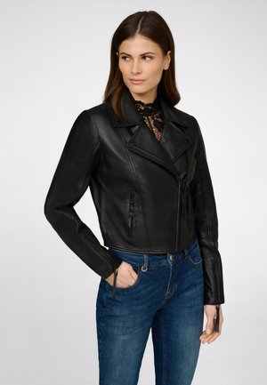 Schwarze Leder-Motorradjacke mit asymmetrischem Reißverschluss, breiten Revers und Reißverschlusstaschen. Über einem Spitze-Top getragen und kombiniert mit blauen Jeans.