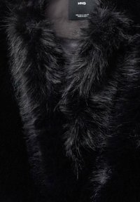 Sort faux fur krave med en blød, fluffy tekstur og et slankt design. Etiketten er synlig i den øverste sektion.