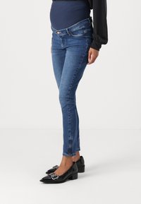 Maternity skinny jeans in dark blue denim with a stretchy waistband, featuring zippers at the ankles and a slim fit throughout the legs.