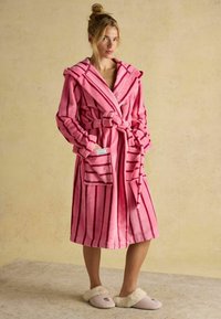Różowa szlafrok w paski z kapturem i paskiem do związania, wykonany z miękkiego materiału; posiada dwie przednie kieszenie. Noszony z jasnoróżowymi kapciami z futrzanym wykończeniem.