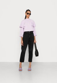 Top curto de lavanda com mangas franzidas, jeans pretos de cintura alta, sandálias roxas tipo slide e uma pequena bolsa preta. Óculos de sol incluídos.