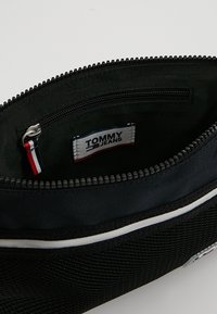 Borsa di stoffa nera con chiusura a zip. L'interno presenta una superficie liscia e un'etichetta con logo. Include una piccola tasca con zip all'interno.