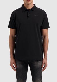 Zwarte polo met een klassieke kraag, korte mouwen en een knoopsluiting met drie knopen. Heeft een subtiele logodetail op de borst. Zacht materiaal.