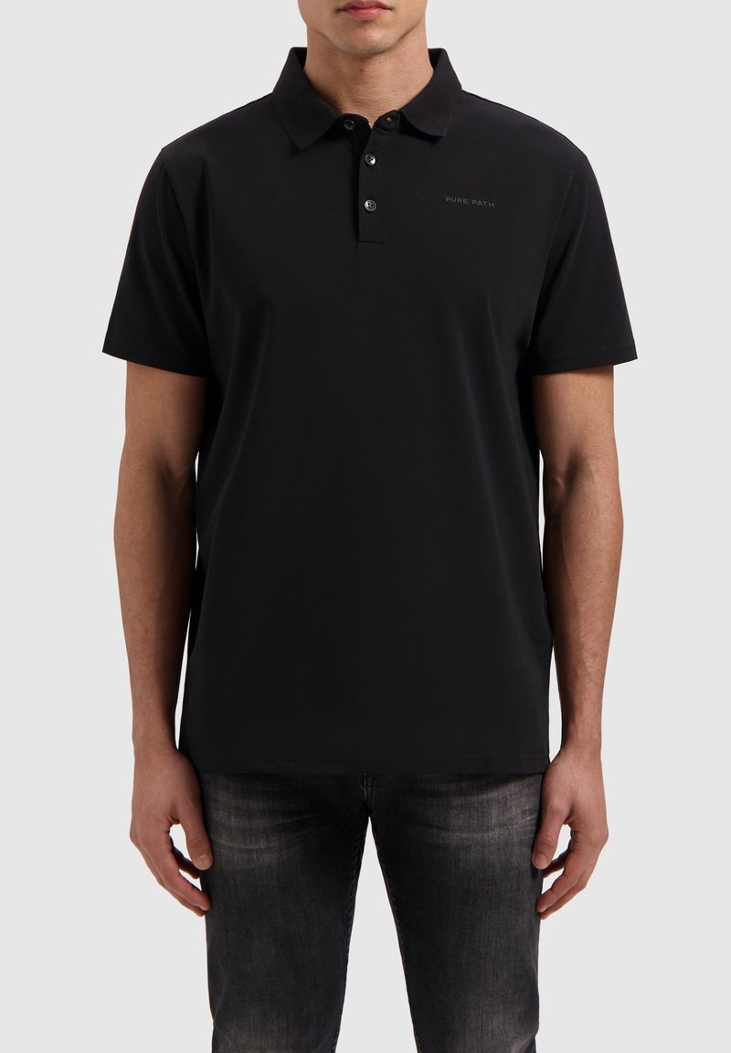 Zwarte polo met een klassieke kraag, korte mouwen en een knoopsluiting met drie knopen. Heeft een subtiele logodetail op de borst. Zacht materiaal.