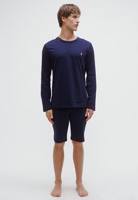 Top azul-marinho de manga comprida e calções até ao joelho feitos de tecido macio e elástico. Detalhe subtil com logótipo no peito. Adequado para roupa de descanso.