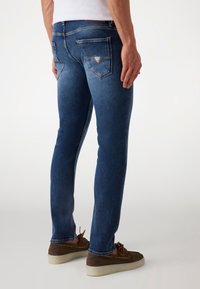 Denim jeans in een middentoon blauw met een slim fit. Kenmerken zijn onder andere twee achterzakken en zichtbare stiksels, gecombineerd met bruine schoenen.